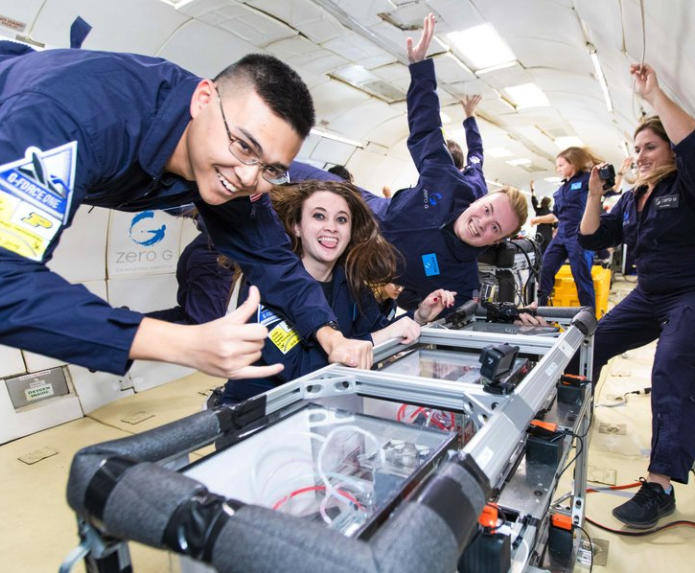 Image Description: Large group of smiling students perform a research experiment while floating inside the ZERO-G plane. Credit: ZERO-G.