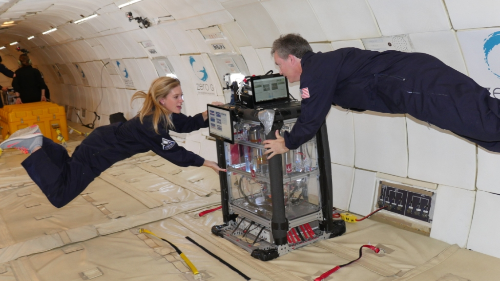 Two researchers float during a ZERO-G flight while holding on to a large rectangular experiment apparatus. This research was conducted by Carthage College. Credit: ZERO-G.