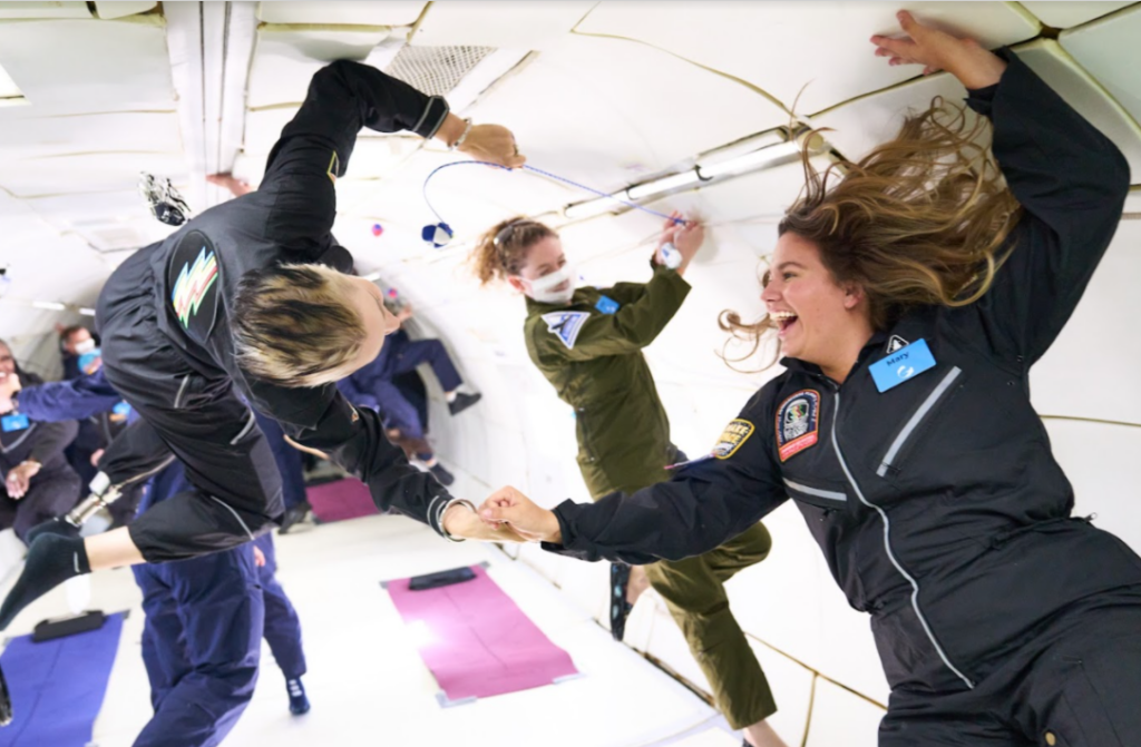 Two ambassadors experiencing zero gravity, holding hands.